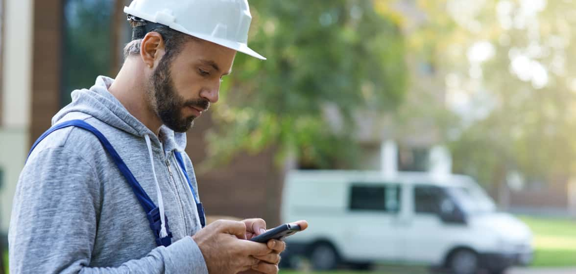 Un ouvrier de construction consulte QuickBooks sur son téléphone à l’extérieur d’une maison sur laquelle il travaille.