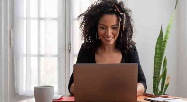 Femme aux cheveux bouclés assise à table, travaillant sur son ordinateur portable
