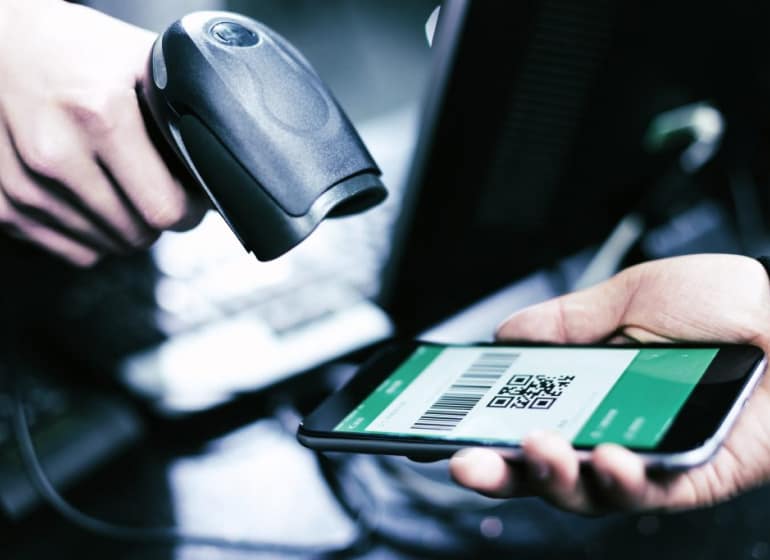 A hand holding a scanner scans a QR code on a smartphone.