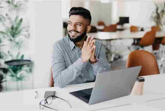 A smiling accountant sitting in a modern open office using QuickBooks Online Accountant on his laptop.