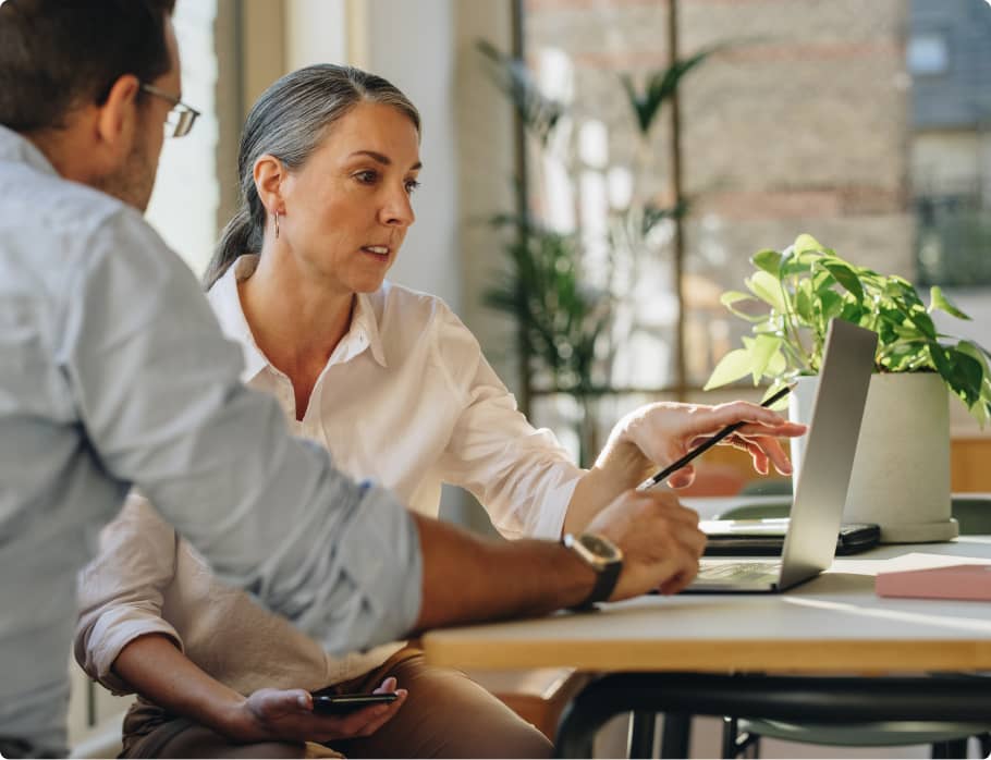 Une femme consulte son comptable et montre son portable sur une table éclairée par le soleil.