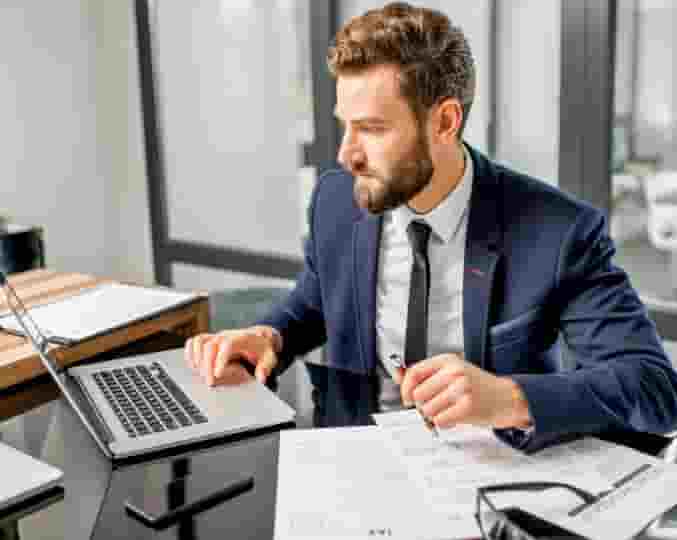 Man in blue suit diligently checking between laptop and papers