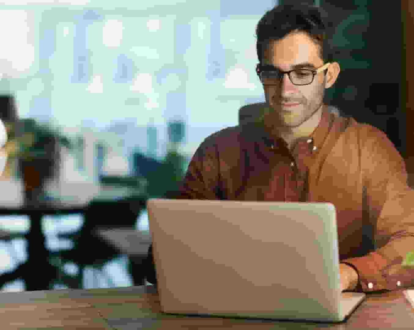 Man in red ochre shirt concentrating while working on laptop