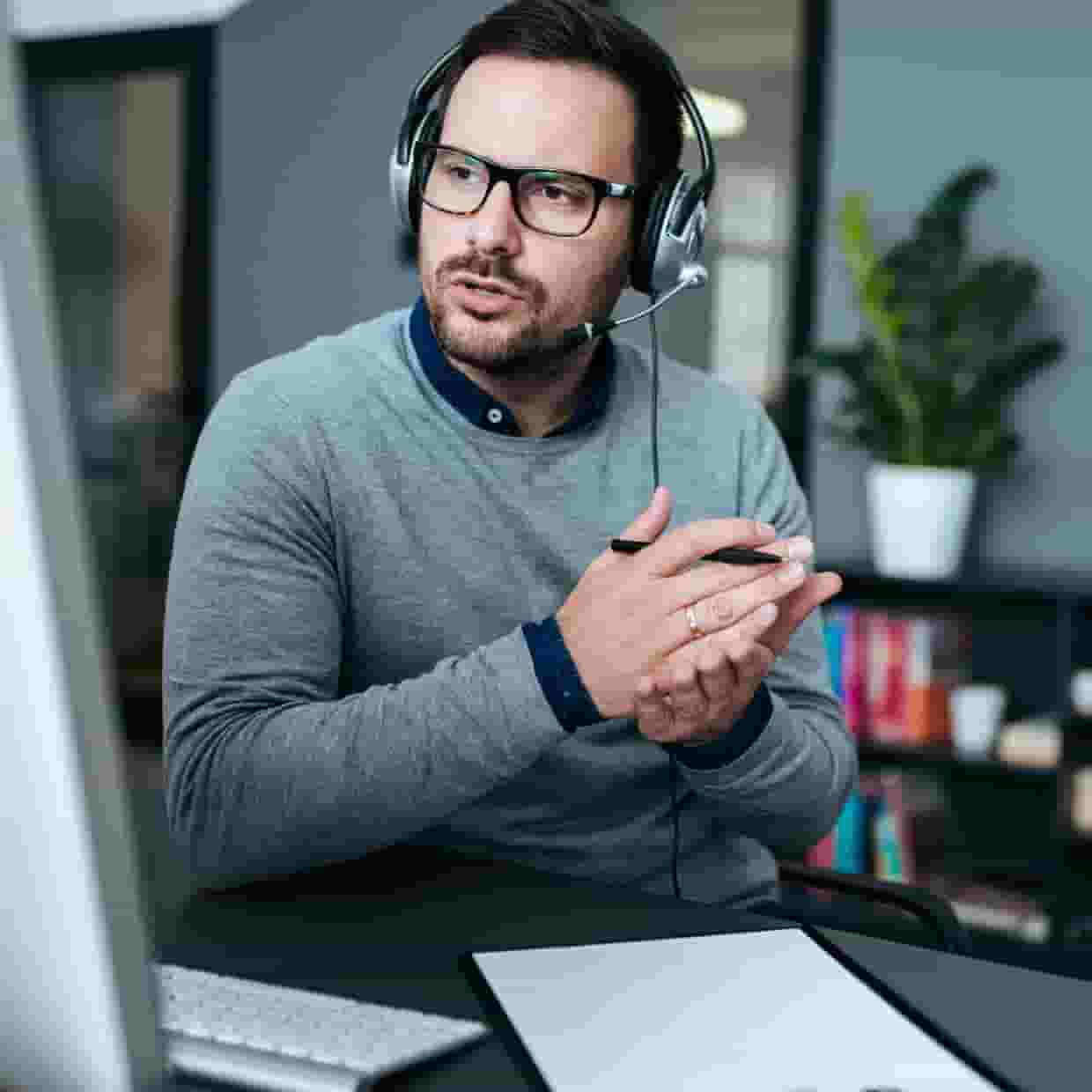 A man in an office wearing a headset and working at computer.