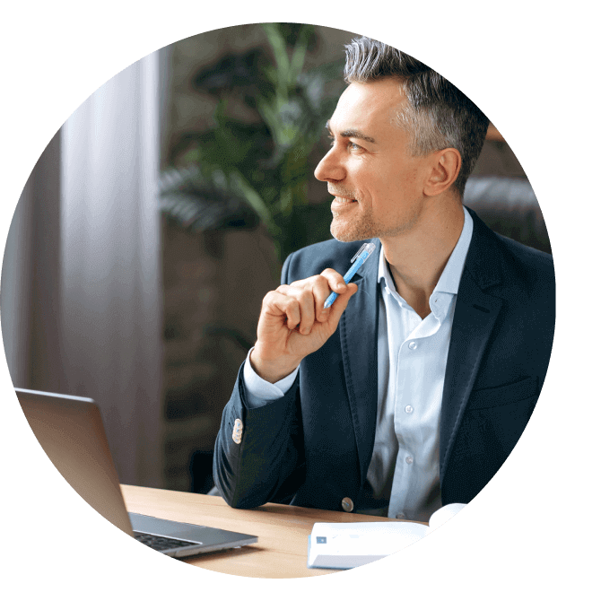 A smiling man wearing a suit looks up from his Apple laptop.