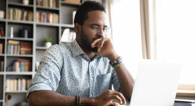 Man deep in thought while holding paperwork and looking at laptop