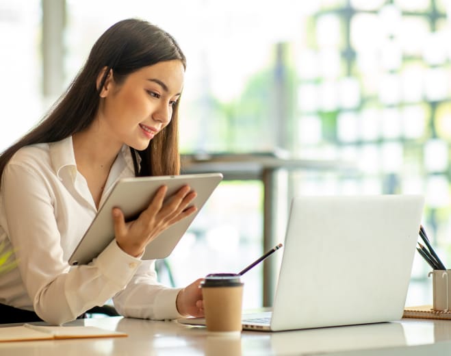 Woman holding iPad checks her laptop