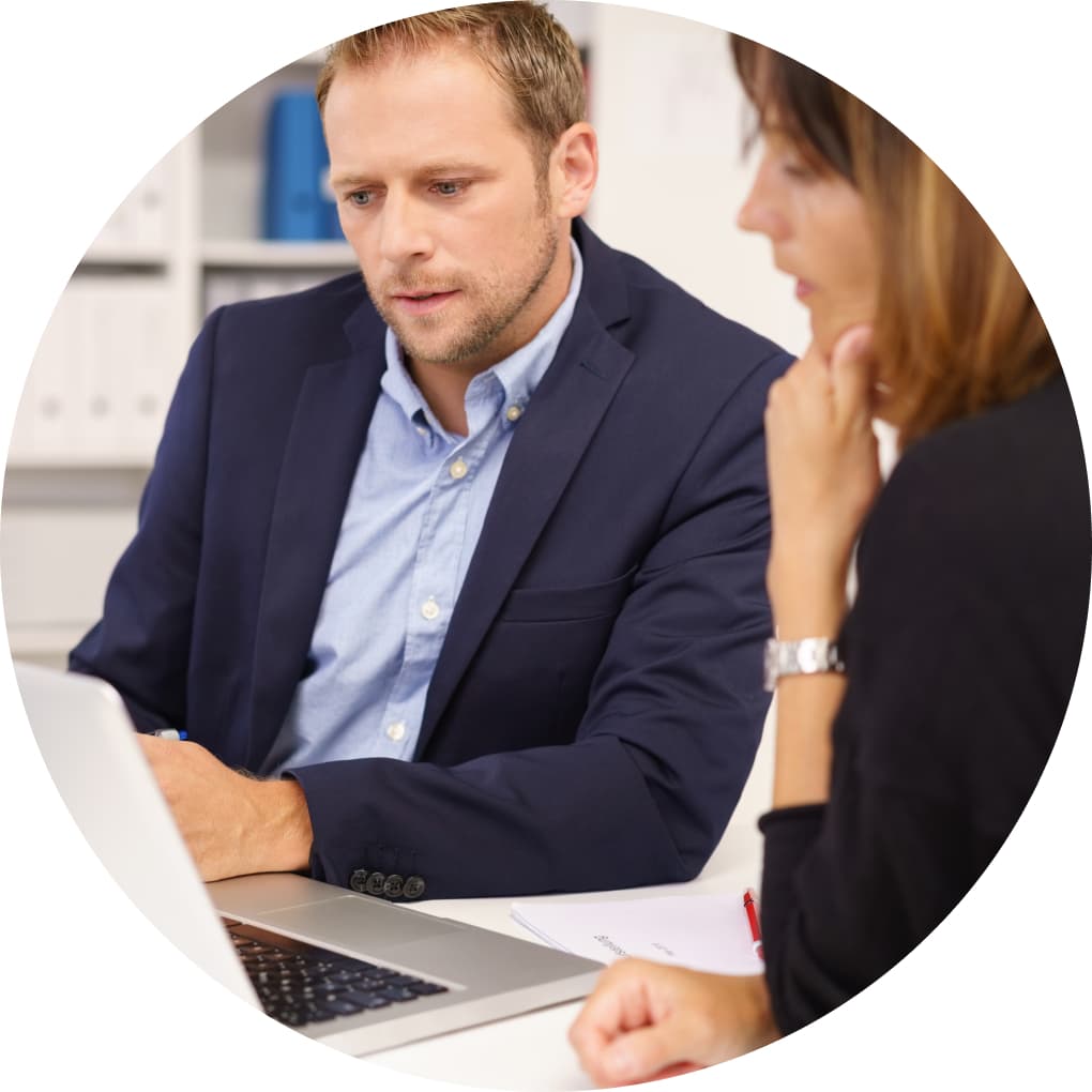 A man in a blue blazer working with a woman, both concentrating on a silver laptop. 