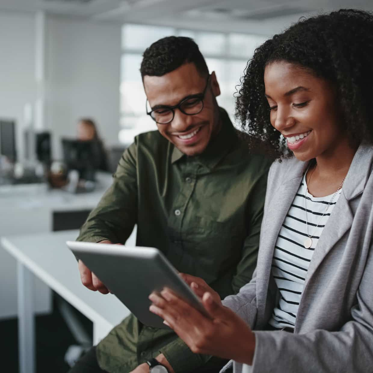 Two people in large office smile while consulting a tablet