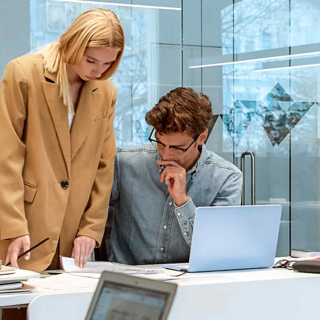 Two people discussing papers on a desk before their laptop.