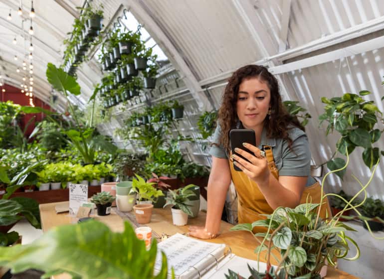 A woman looks at her smartphone inside of her plant shop.
