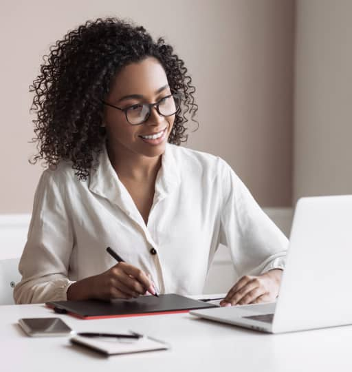 Woman with glasses and curly hair using tablet and laptop