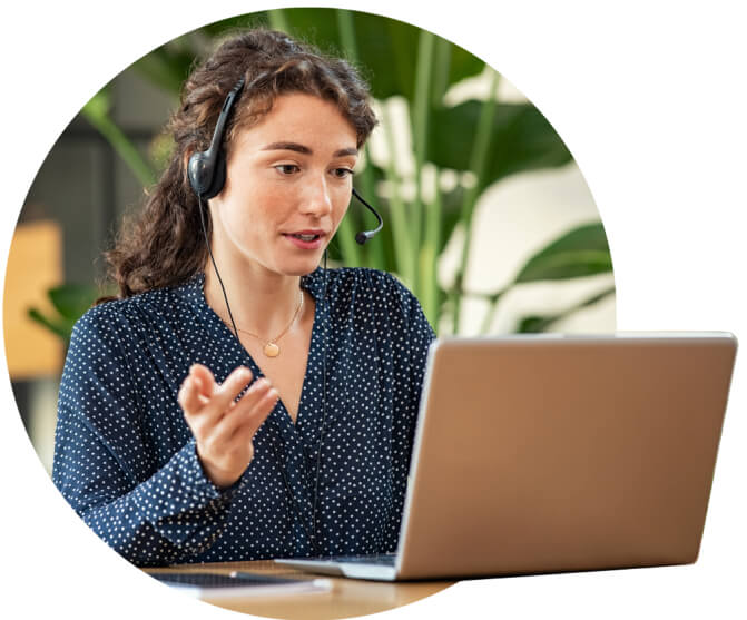 A woman wearing a headset talks and gestures while on a call on her laptop