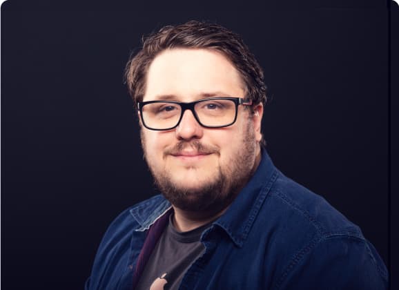 A person with glasses and a tie is leaning against a wall.