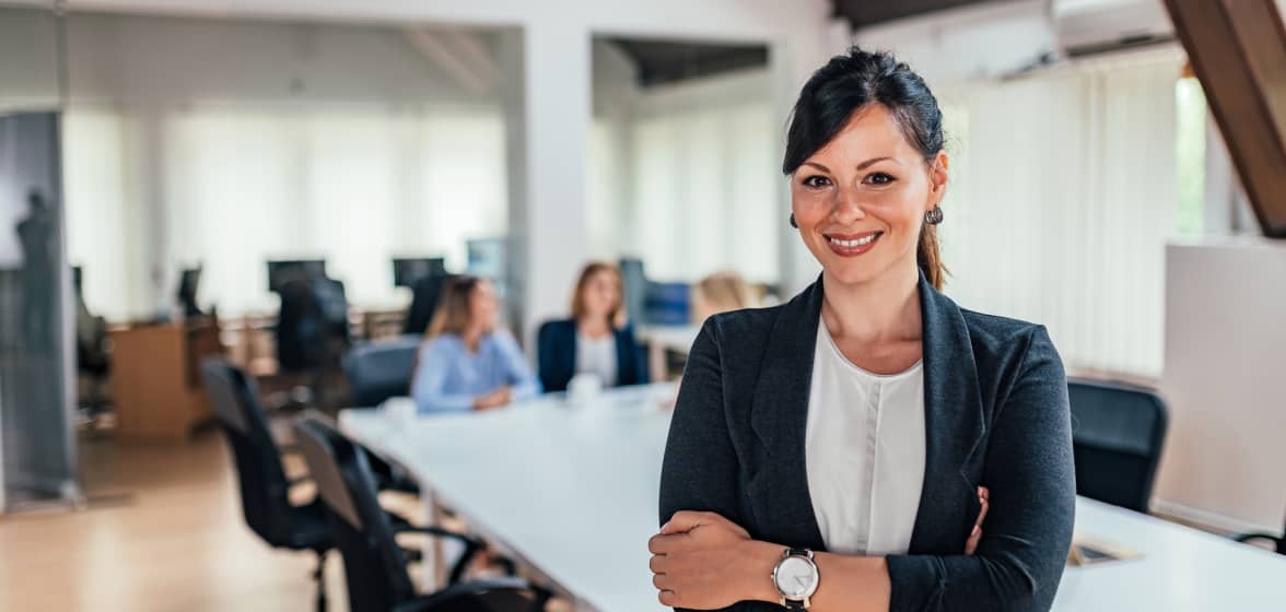 A person smiles as she stands in front of a laptop.