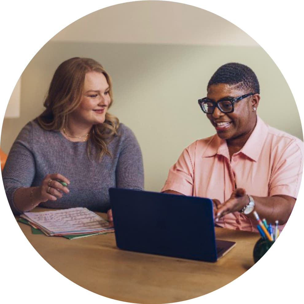 A person and person sitting at a table with a laptop.