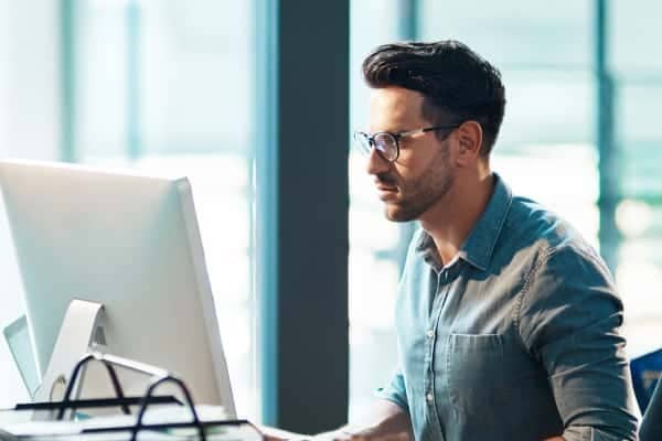 A person in a white shirt and glasses looking at a laptop.