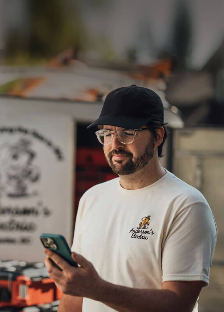 A person wearing a hat and glasses is holding a cell phone.