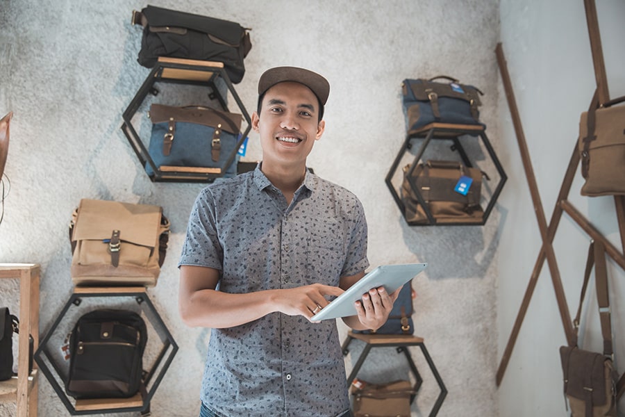 Un hombre emprendedor sonriendo con una tablet en la mano y con mostradores con maletas detrás de él