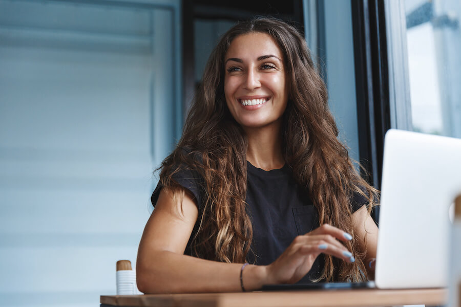 Una mujer frente a un computador portatil sonriendo al revisar los reportes financieros de su negocio