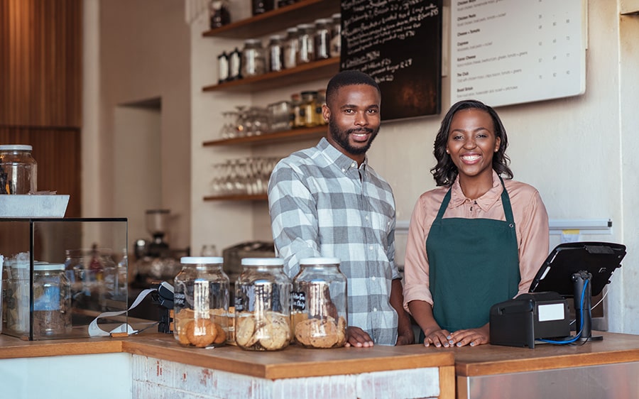 Dos emprendedores sonriendo parados detrás de la barra de su cafetería