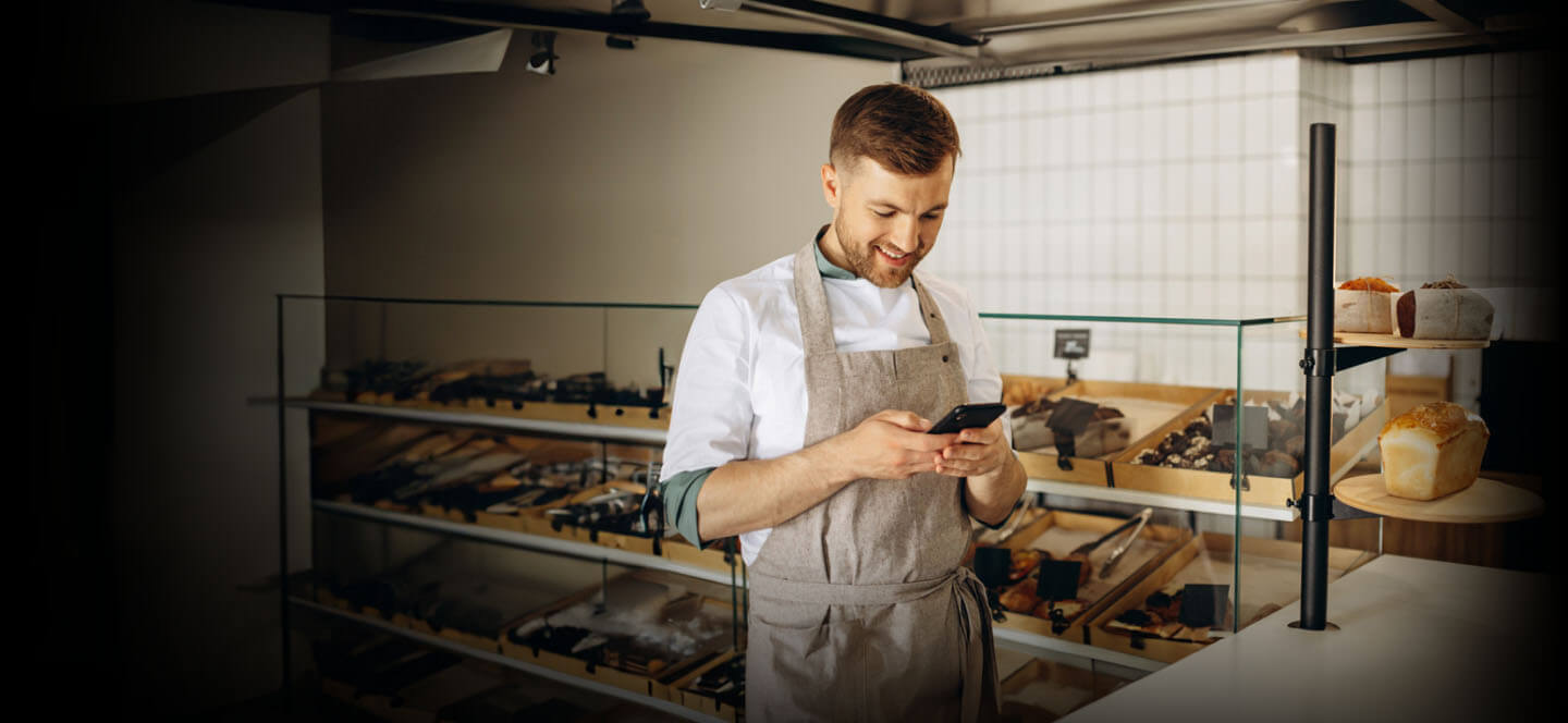 A person in a bakery holding a cell phone.