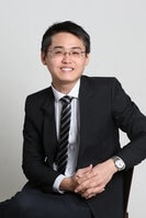 A person in glasses and a tie smiles.