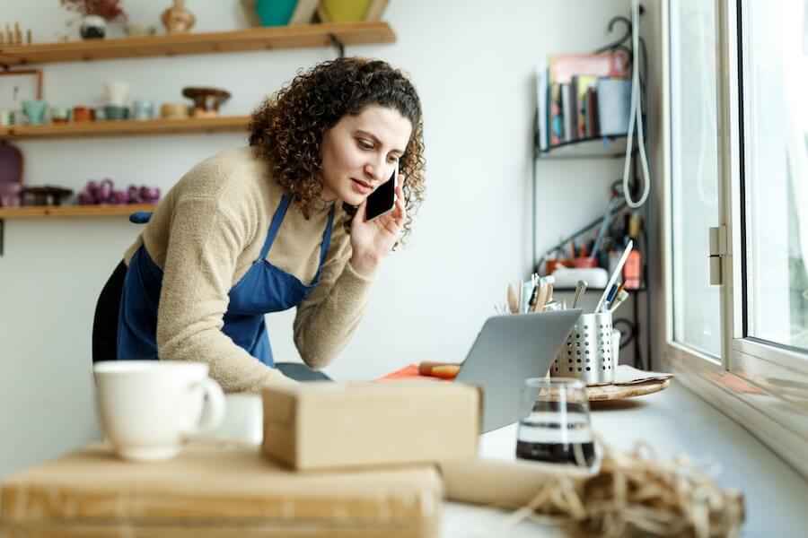 Small business owner taking phone orders and putting them on her laptop.