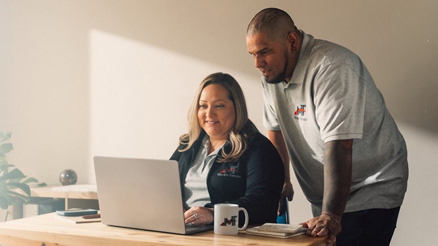 Two people are sitting at a table with a laptop, researching small business insurance claims.