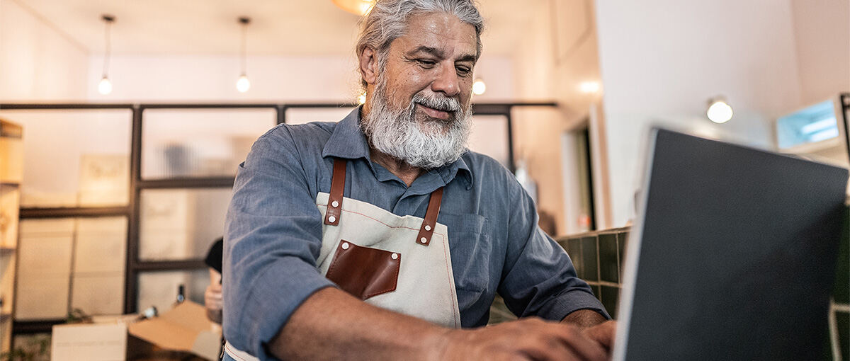 A man smiling while sitting at a table typing on a laptop