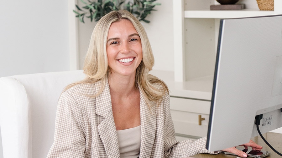 A person smiling while sitting at a desk with a laptop.