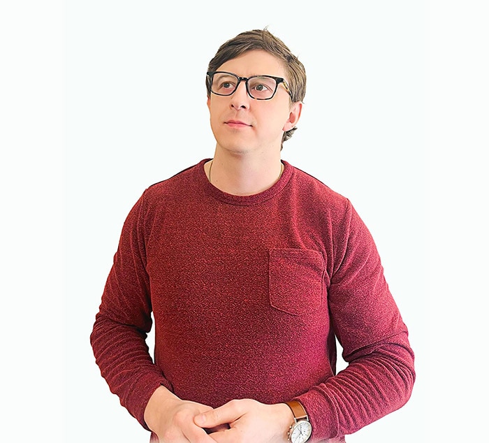 A person wearing glasses and a sweater with a red bow tie.