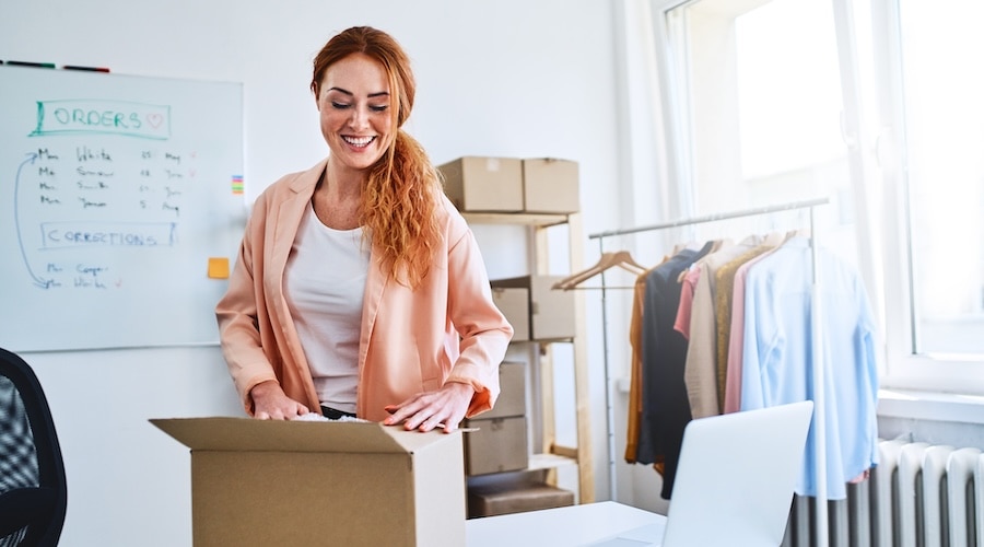 A person in a blazer smiles as she packs an online order.