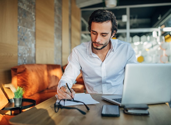 Man writing in notepad with laptop