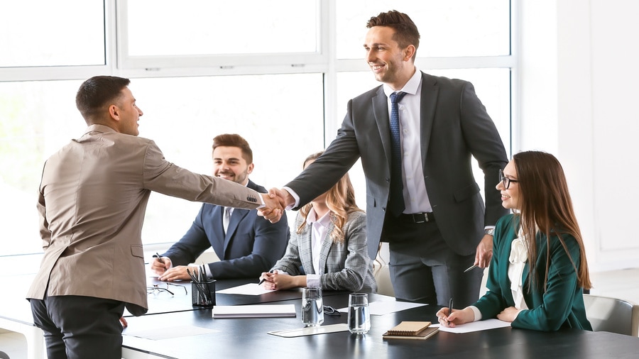 Business professionals greeting each other in modern office conference room.