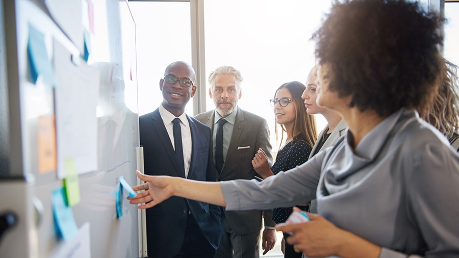 A group of business people around a whiteboard brainstorming how to grow a multi-million dollar business.