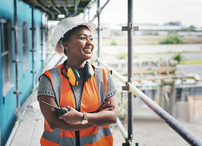 A person in a construction site smiles while talking on her phone.