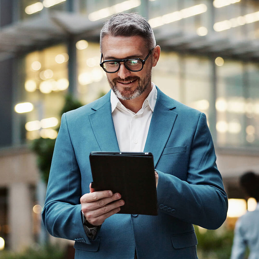 A person wearing a suit and glasses holding a tablet.