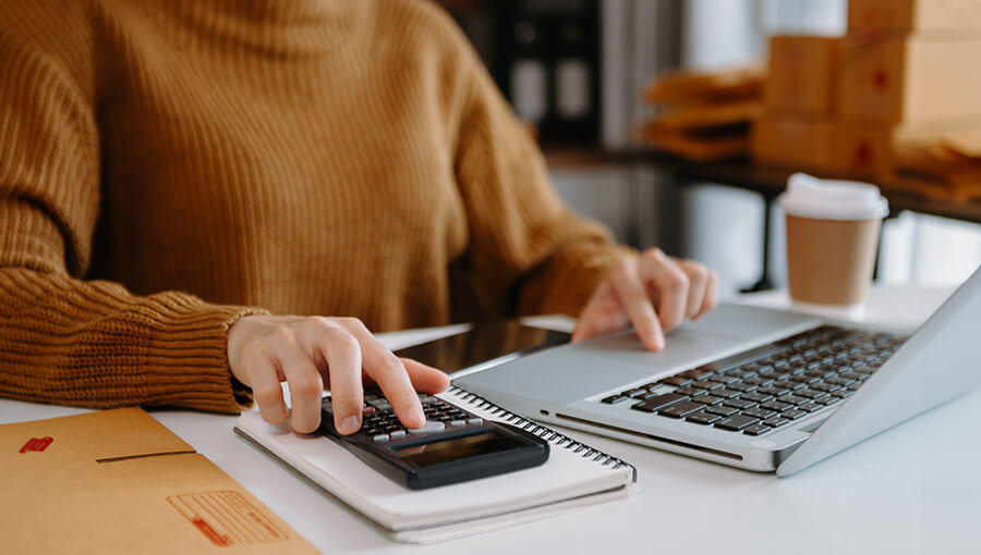 A closeup of hands on a laptop and on a calculator.