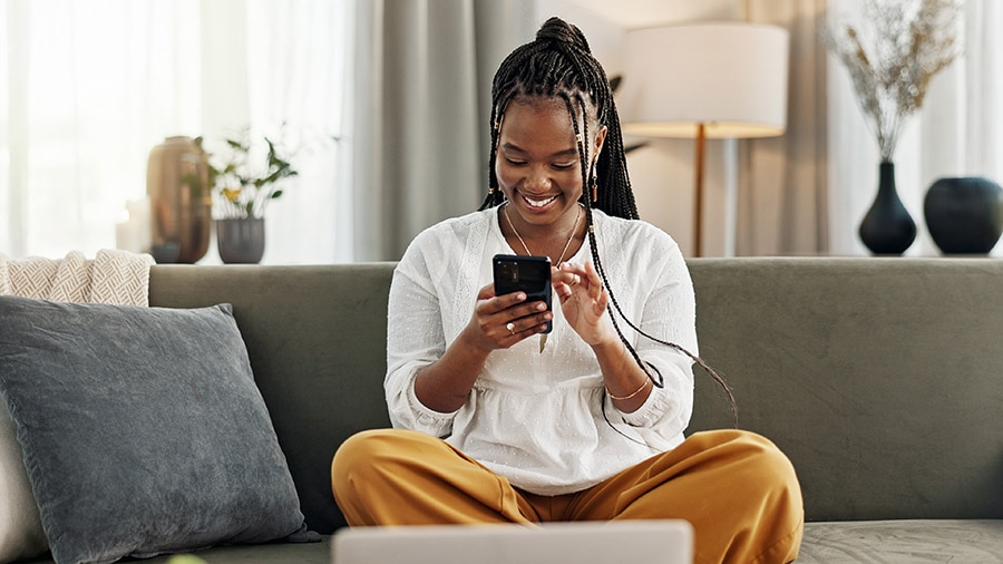 A person sitting on a couch holding a smart phone, checking out new features on QuickBooks Online
