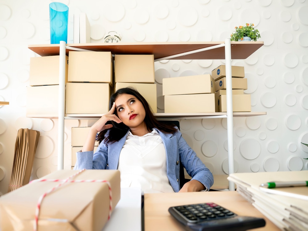 Woman sitting at her desk looking pensive and tired while being surrounded by boxes and packing supplies.