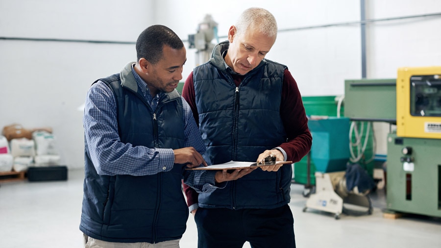 two men talking and pointing to a clipboard inside a warehouse