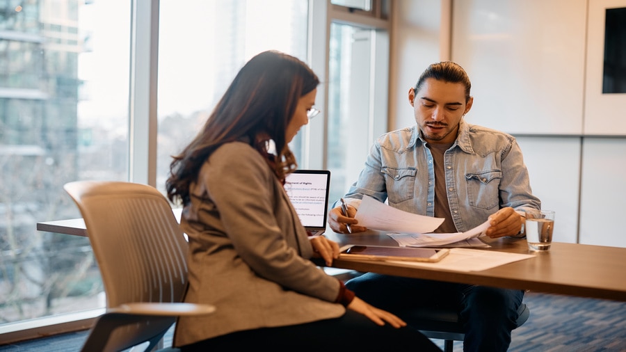 Two coworkers reviewing and signing documents together at a table in a modern office.