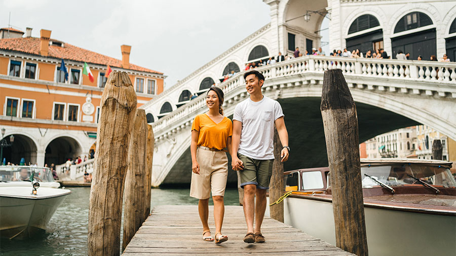 Loving couple on vacation in Venice, Italy - Millennials visiting the famous Rialto Bridge while walking on the wooden pier