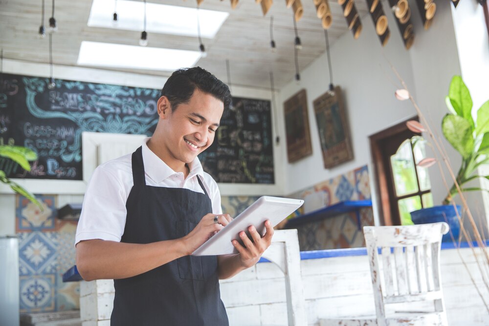 Business owner standing in restaurant reviews information on tablet while smiling
