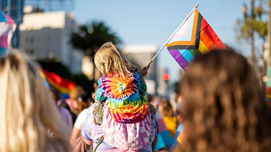 A person walking down a street holding a rainbow colored flag.