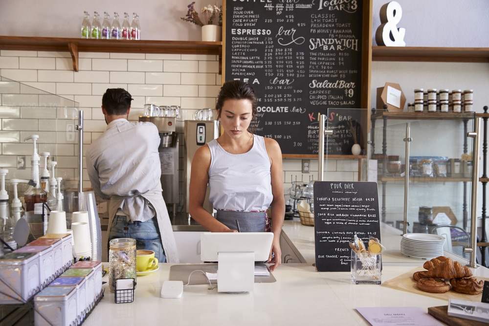 Small business owner working in cafe reads point of sale system.
