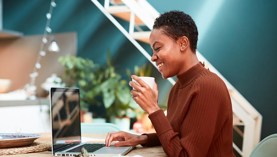 A woman sits in front of a laptop holding a coffee, indicating she's researching W-9 vs 1099.