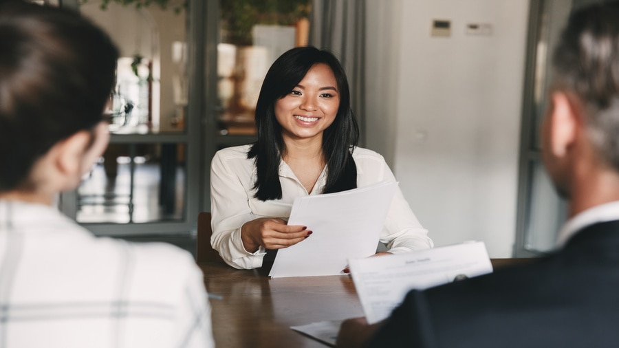 A woman holding documents and speaking with two people seated across from her during a job interview.