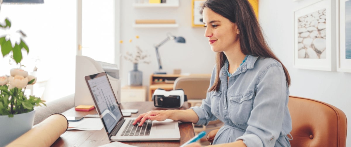 A bookkeeper sits at a desk while using a laptop and writing notes.